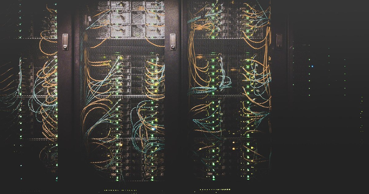 Racks de servidores com cabos e LEDs verdes acesos num data center escuro