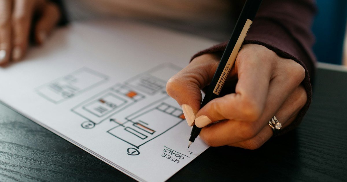 Mão desenhando wireframes de interface a caneta sobre papel