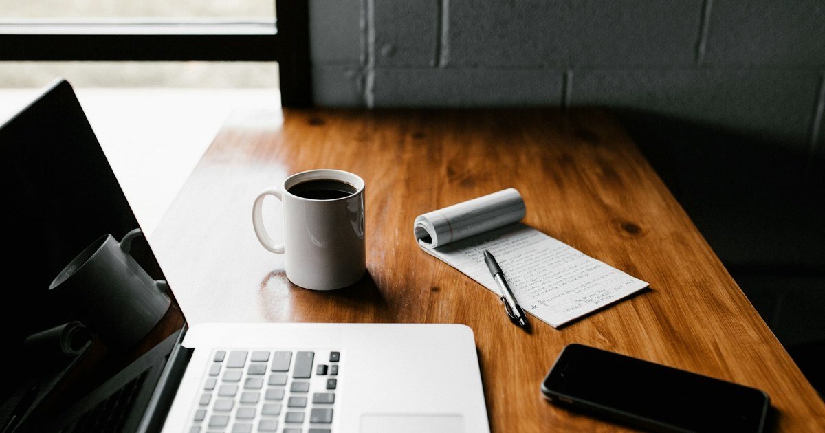 Notebook, caderno de anotações e xícara de café sobre mesa de madeira